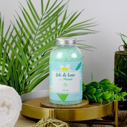 Sels de bain parfumés au monoï sur un plateau doré avec des plantes vertes.