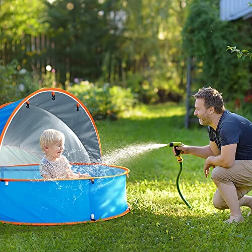 Un enfant joue dans une piscine avec un adulte utilisant un tuyau d'arrosage.
