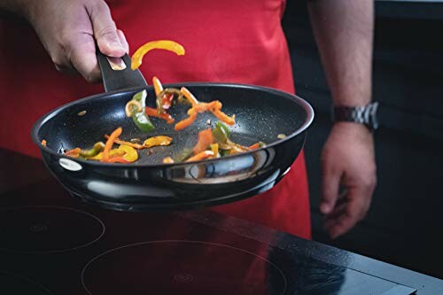 Main tenant une poêle avec des légumes sautés.