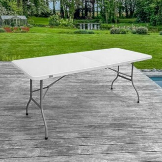 Table pliante blanche sur une terrasse en bois avec jardin en arrière-plan.