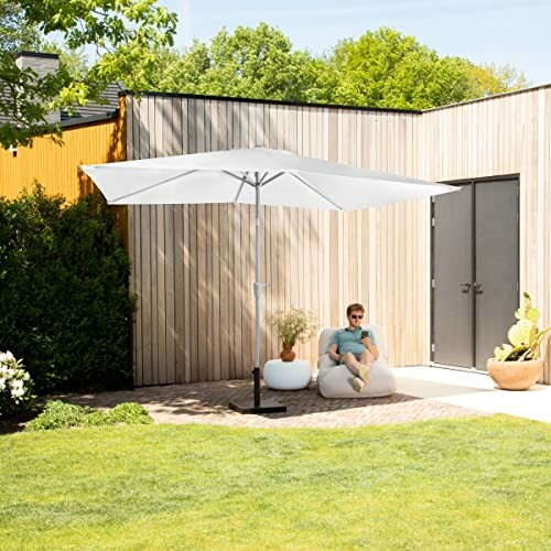 Homme assis sous un parasol blanc dans un jardin.