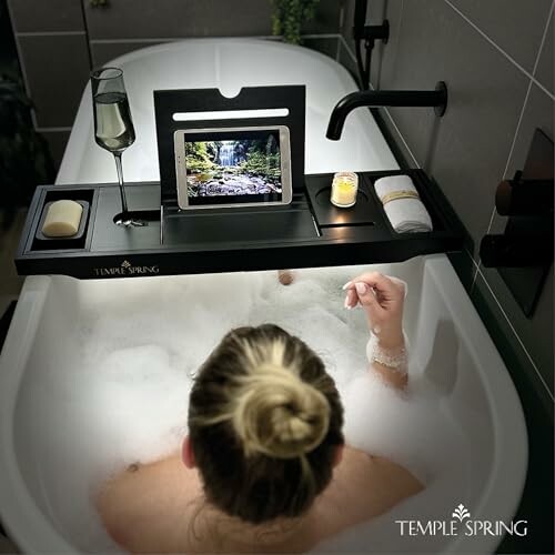 Personne prenant un bain avec une tablette, un verre et une bougie.
