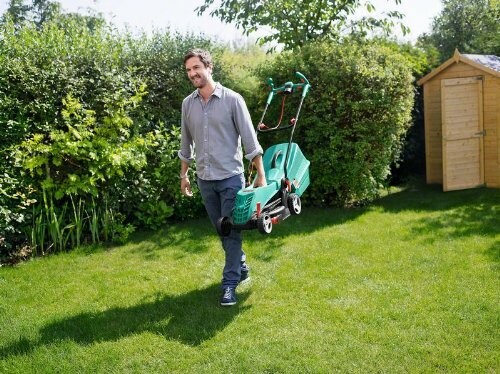 Homme portant une tondeuse à gazon dans un jardin