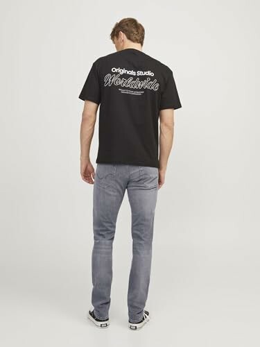 Homme portant un t-shirt noir avec inscription au dos et un jean.