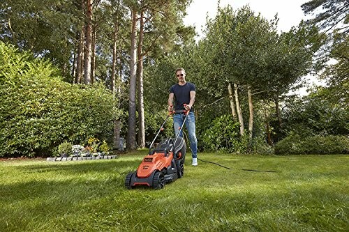 Homme tondant la pelouse avec une tondeuse électrique dans un jardin verdoyant.