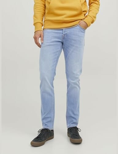 Homme portant un sweat jaune et un jean clair.