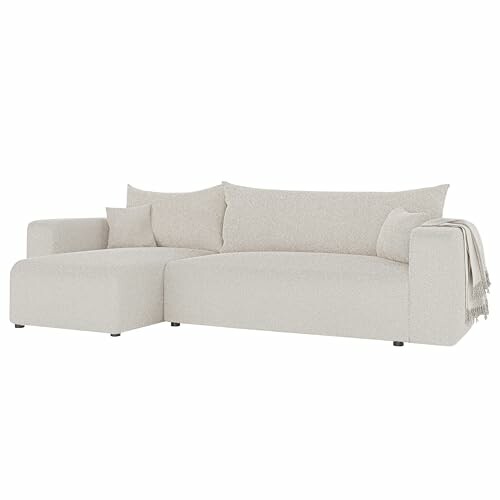 Canapé sectionnel beige minimaliste avec coussins et couverture.