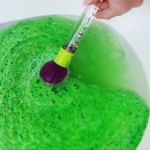 Main mélangeant un bain moussant vert avec un pinceau.
