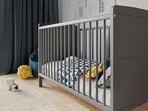 Lit de bébé gris moderne dans une chambre avec des jouets et des coussins.