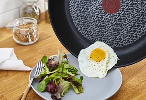 Poêle antiadhésive avec œuf au plat et salade verte.