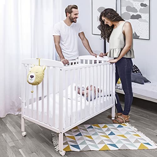 Un couple regarde un bébé dans un berceau blanc.