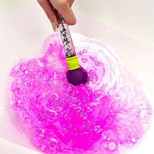 Main mélangeant de la peinture rose dans l'eau avec un pinceau.