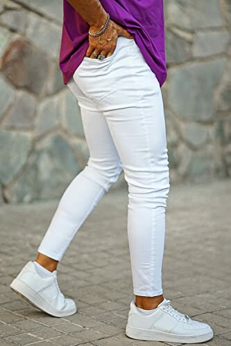 Personne portant un pantalon blanc et un t-shirt violet avec des baskets blanches.