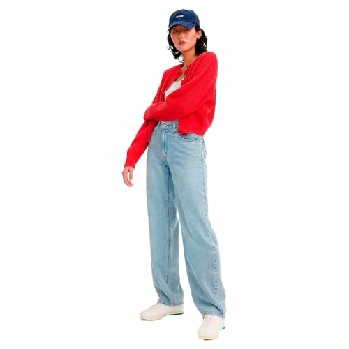 Femme portant un cardigan rouge, un pantalon en jean et une casquette.