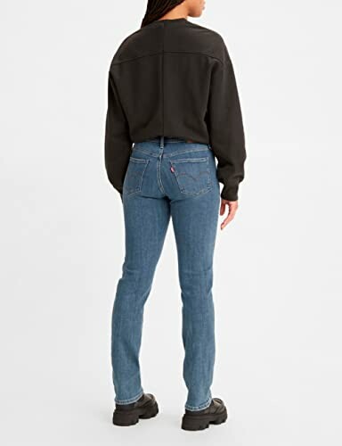 Femme portant un jean bleu et un pull noir.