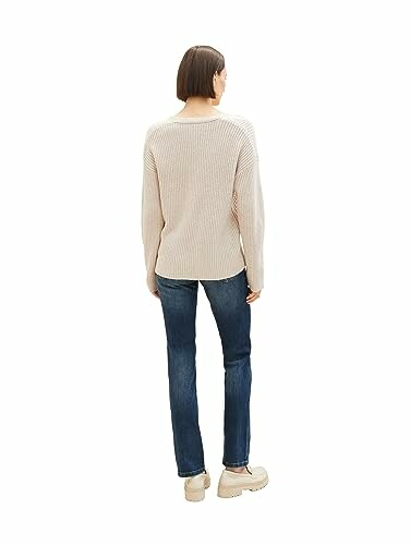 Femme portant un pull beige et un jean, vue de dos.