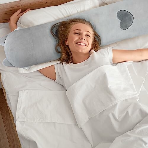 Femme souriante allongée dans un lit avec un oreiller gris.