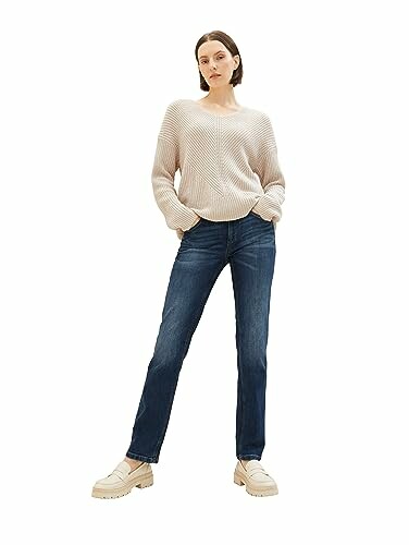 Femme portant un pull beige et un jean bleu.