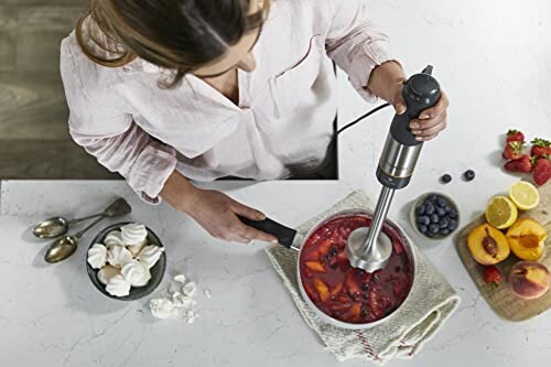 Femme utilisant un mixeur plongeant pour préparer une sauce aux fruits.